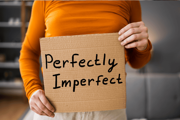 Photo of a person holding a cardboard with ''perfectly imperfect'' written on it.