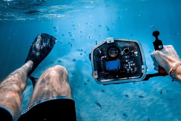 man bathing under the sea while holding black camera