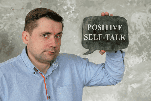 A man holding up a slate written Positive Self-Talk.