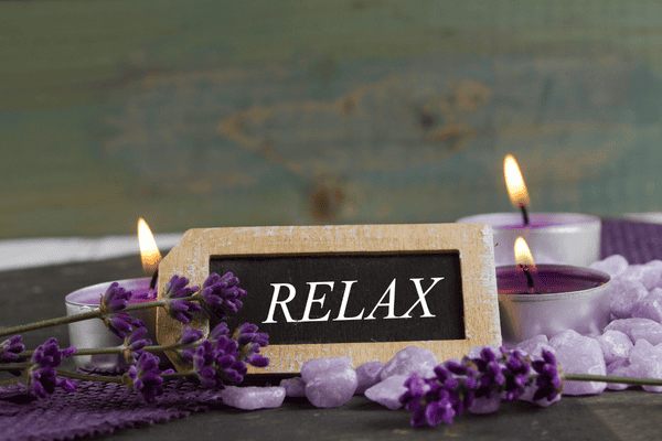 relax written on a small black slate with purple candles lit.