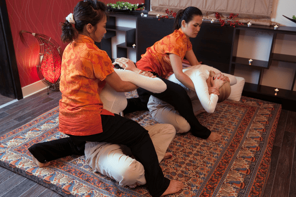 2 people getting Thai massage from 2 therapists.