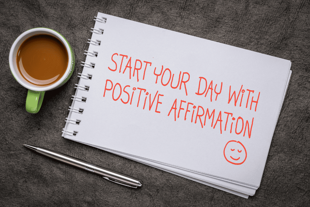 Start your day with positive affirmation written on a notepad. Pen and coffee mug nearby.