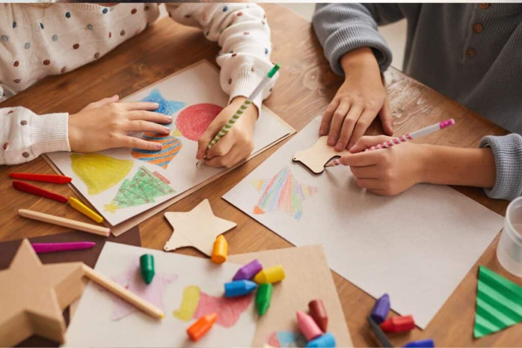 Two children engage in self-care activities, drawing colorful shapes on paper with crayons.