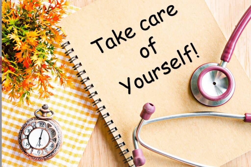 A spiral notebook with "Take care of Yourself!" written on it lies beside a stethoscope, pocket watch, and an autumn-themed plant on a checkered cloth, reminding you to include evening self-care routines in your daily life.