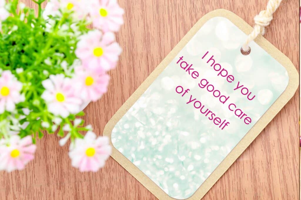 A bouquet of white and pink flowers sits on a wooden surface, accompanied by a tag with the message "I hope you take good care of yourself," offering a gentle reminder to embrace evening self-care routines.