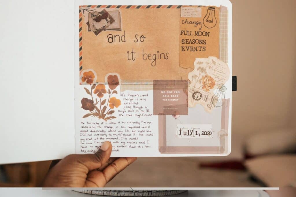 A hand holds a notebook page featuring artistic scrapbook-style elements, text about life events, and a date reading "July 1, 2020.