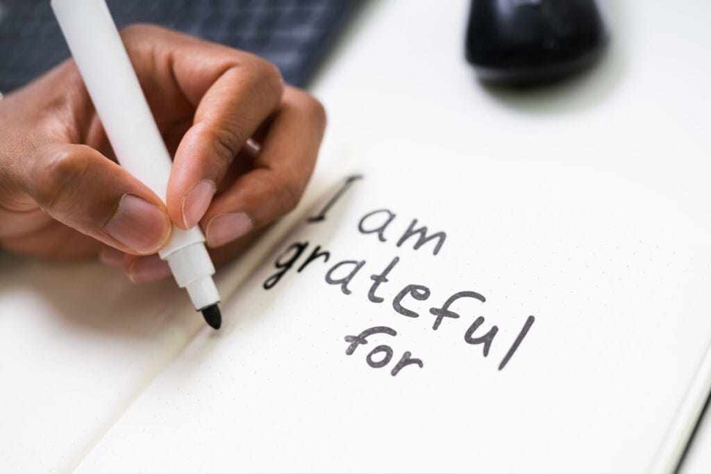 Hand writing "I am grateful for" with a black marker on a dotted notebook page.