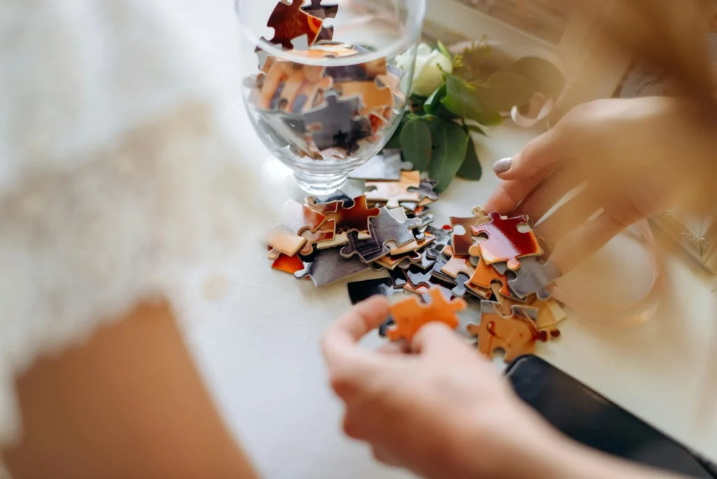 A close-up of hands sorting puzzle pieces on a table, with additional pieces in a glass jar, creates a serene self-care ritual.