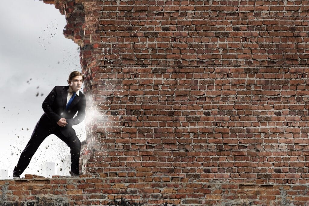 A person in a suit is breaking through a large brick wall with force, much like tackling life’s obstacles with the determination of pursuing journal prompts, causing debris to scatter.