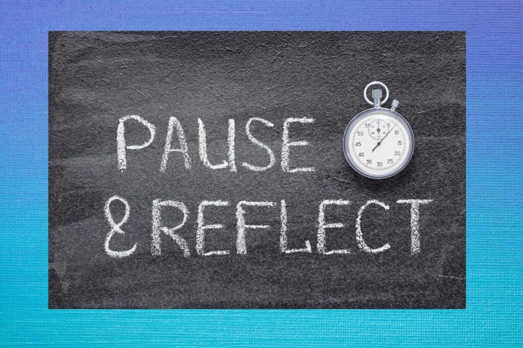 A chalkboard displays "Pause & Reflect," with journal prompts neatly sketched around a stopwatch resting beside the text.