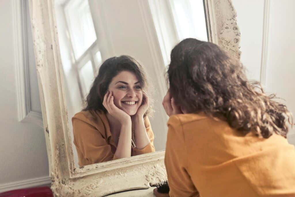 A lady looking into the mirror and smiling,