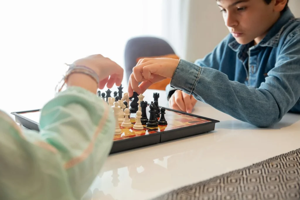 Feeling lost in the game, two people engage in a thoughtful match of chess on a checkered board. One moves a black pawn, contemplating their next strategy, while the other calmly adjusts a white piece, seeking clarity and purpose with each calculated move.