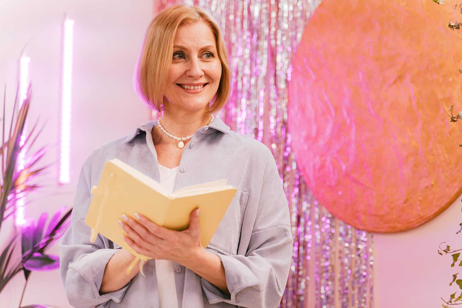 Smiling mature woman enjoying journaling in a vibrant, artistic indoor setting.