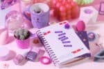 A colorful desk showcases a planner labeled "Me time" for journaling for self-care, paired with a cat-themed mug, cactus, nail polish, and decorative items on a pink background.